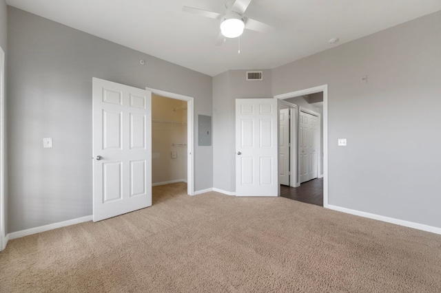 unfurnished bedroom with visible vents, a walk in closet, electric panel, carpet, and baseboards