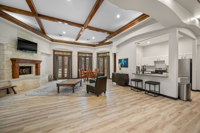 living area featuring beamed ceiling, coffered ceiling, a high ceiling, a fireplace, and light wood finished floors