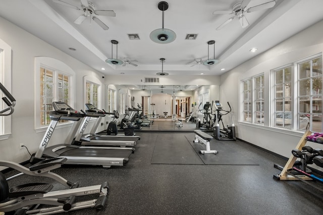 exercise room with a tray ceiling, baseboards, visible vents, and ceiling fan