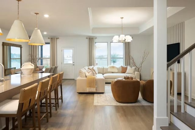 living area featuring wood finished floors, a tray ceiling, an inviting chandelier, recessed lighting, and stairs