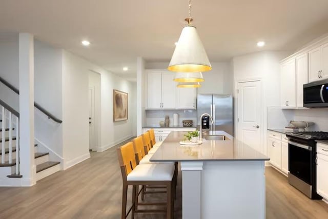 kitchen with light wood-type flooring, pendant lighting, a center island with sink, white cabinetry, and appliances with stainless steel finishes