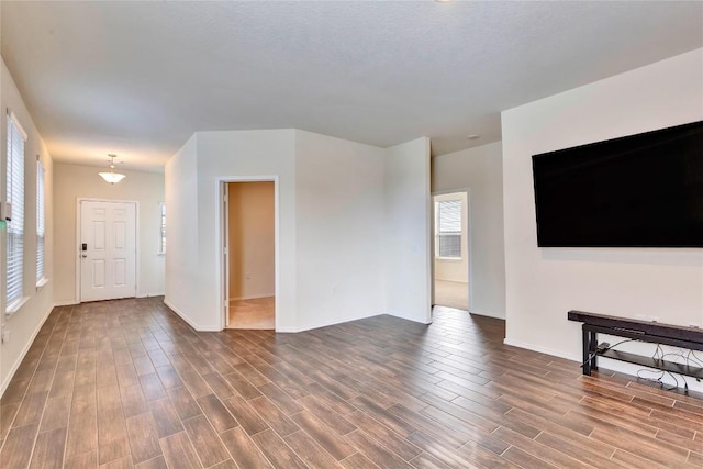 unfurnished living room featuring baseboards, a textured ceiling, and dark wood finished floors