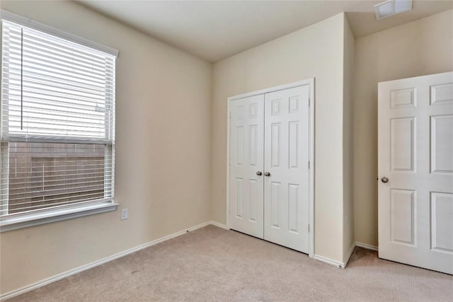 unfurnished bedroom featuring light colored carpet, visible vents, a closet, and baseboards