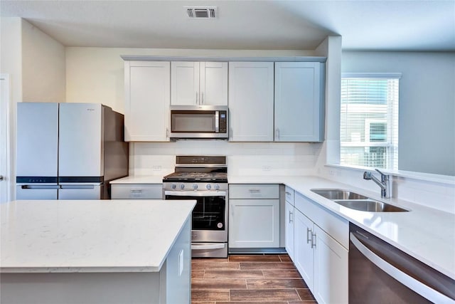 kitchen featuring visible vents, light stone countertops, wood tiled floor, stainless steel appliances, and a sink