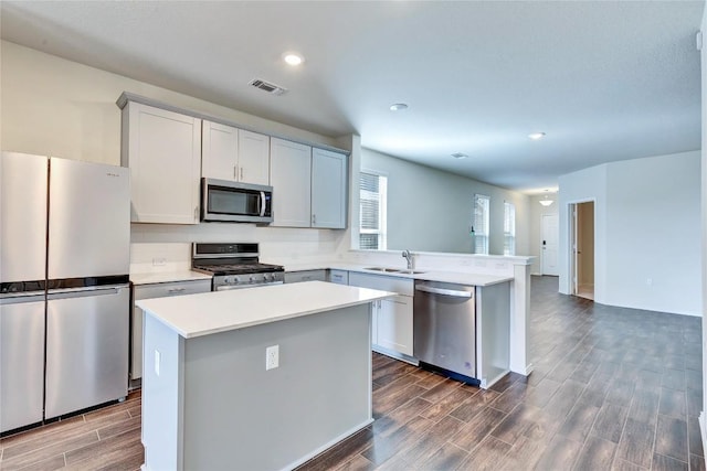 kitchen featuring wood finish floors, a peninsula, stainless steel appliances, light countertops, and tasteful backsplash