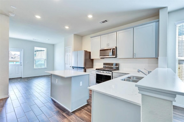 kitchen with visible vents, a kitchen island, light countertops, stainless steel appliances, and a sink