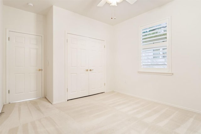 unfurnished bedroom featuring a closet, light colored carpet, baseboards, and ceiling fan