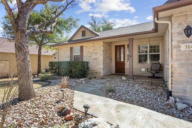 entrance to property featuring stone siding, a porch, and a shingled roof