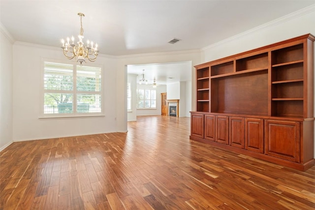 unfurnished living room with a glass covered fireplace, a notable chandelier, dark wood finished floors, and crown molding