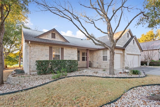 view of front facade with a front lawn, driveway, stone siding, an attached garage, and a shingled roof