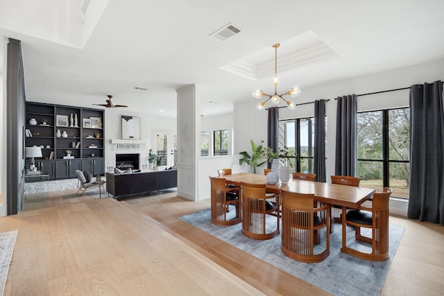 dining area featuring light wood finished floors, visible vents, a large fireplace, and a tray ceiling