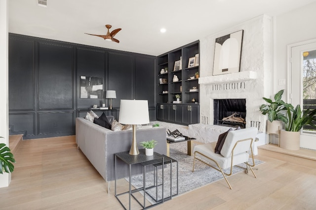 living room with visible vents, built in shelves, a decorative wall, light wood finished floors, and a premium fireplace