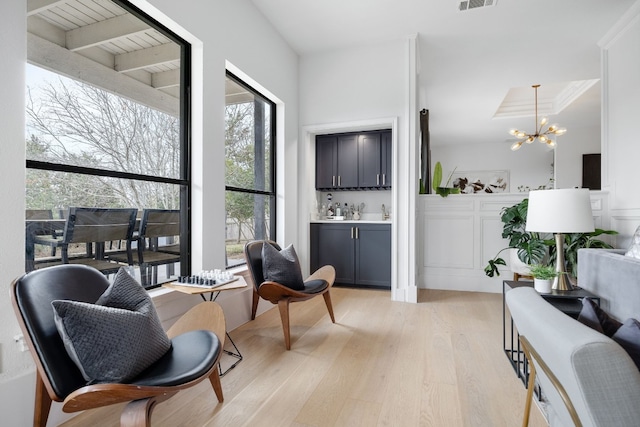 sitting room featuring visible vents, a notable chandelier, a bar, and light wood finished floors