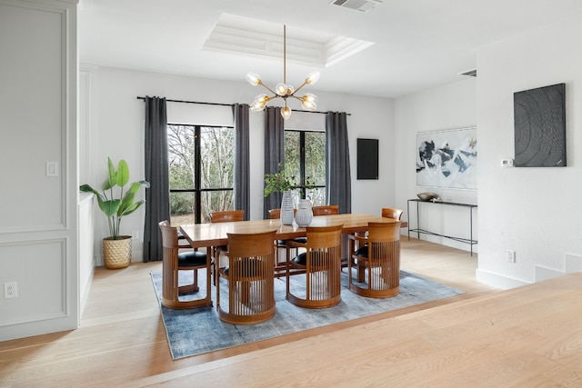 dining space with baseboards, visible vents, light wood-style flooring, a raised ceiling, and a notable chandelier