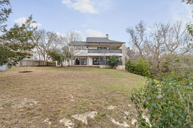 rear view of house with a yard, a chimney, a balcony, and fence