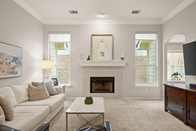 carpeted living area featuring a tiled fireplace, baseboards, visible vents, and ornamental molding