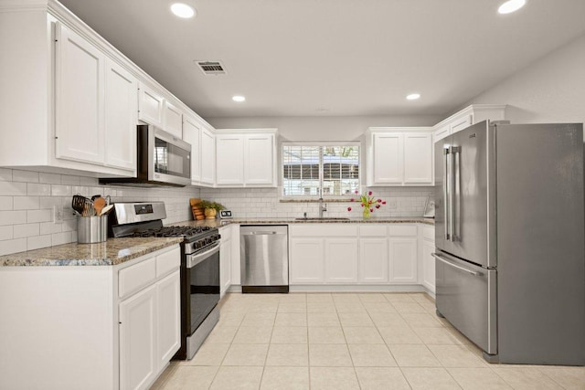 kitchen with light stone countertops, visible vents, a sink, white cabinets, and appliances with stainless steel finishes