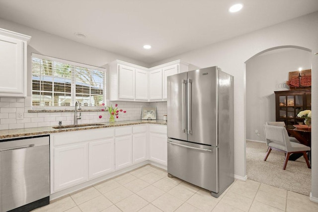 kitchen with arched walkways, backsplash, appliances with stainless steel finishes, and a sink