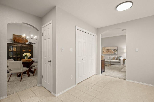 corridor featuring baseboards, arched walkways, a notable chandelier, and light carpet