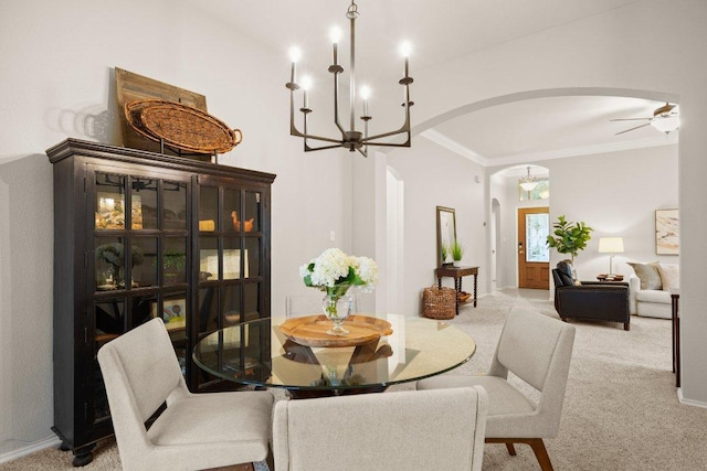 dining space featuring arched walkways, carpet flooring, ceiling fan with notable chandelier, and ornamental molding