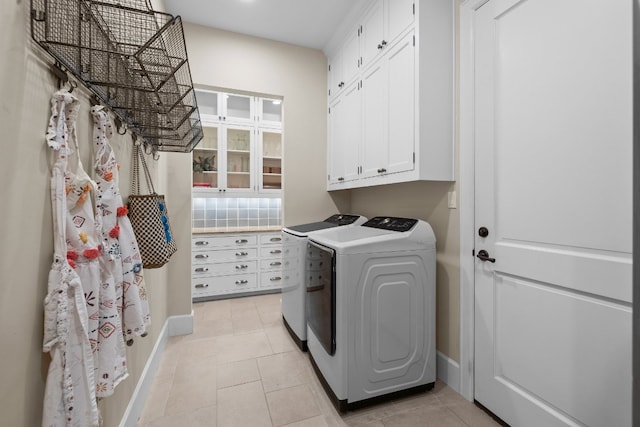 laundry area featuring light tile patterned floors, baseboards, cabinet space, and separate washer and dryer