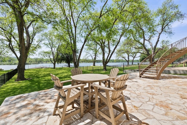 view of patio with a water view, outdoor dining space, stairs, and fence