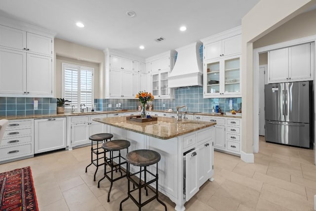 kitchen with custom range hood, white cabinets, and freestanding refrigerator