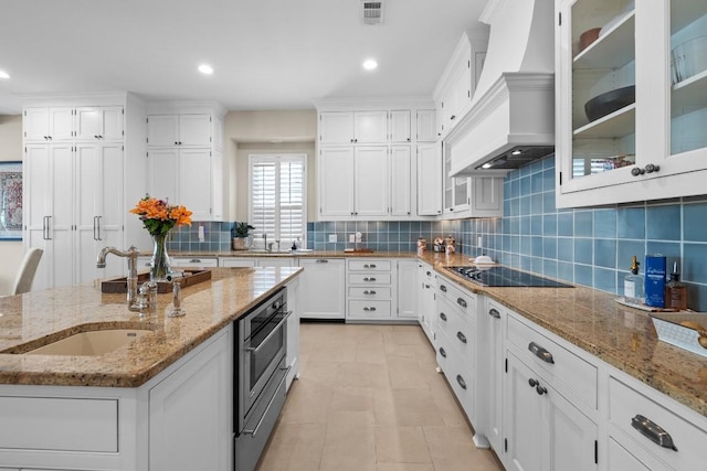 kitchen with a sink, white cabinetry, black electric stovetop, and premium range hood