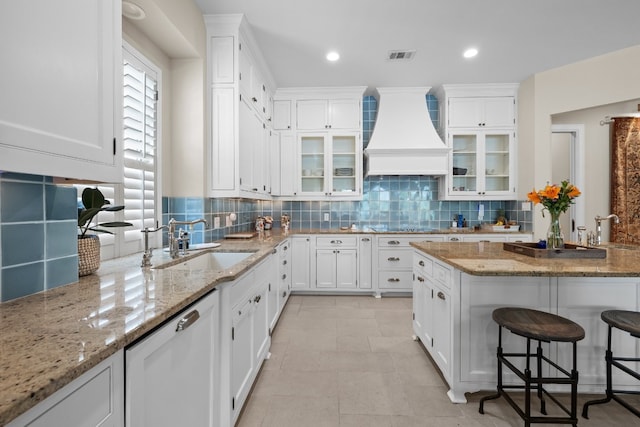 kitchen featuring a breakfast bar area, white dishwasher, custom exhaust hood, white cabinetry, and a sink