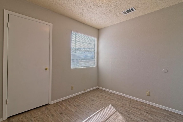 empty room featuring visible vents, baseboards, a textured ceiling, and wood finished floors