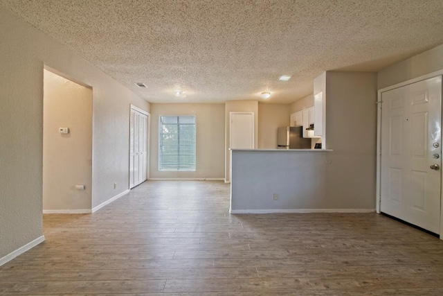 unfurnished living room featuring visible vents, wood finished floors, baseboards, and a textured ceiling