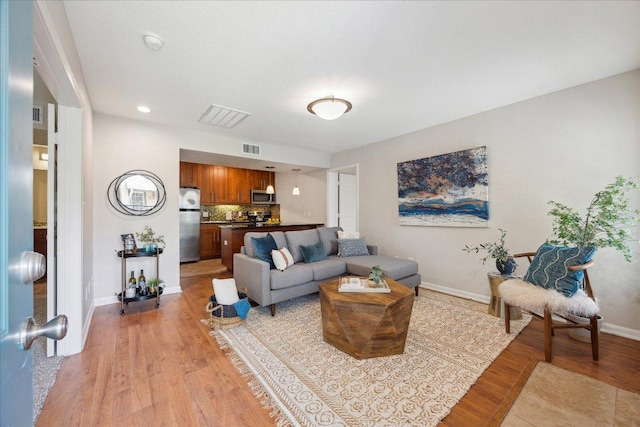 living room featuring visible vents, light wood-type flooring, and baseboards