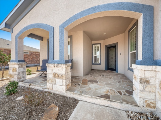 entrance to property featuring covered porch, stone siding, and stucco siding