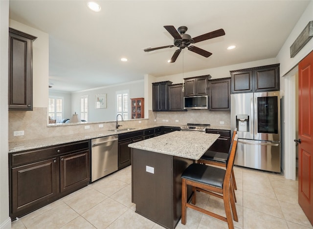 kitchen featuring a breakfast bar area, light tile patterned flooring, a sink, stainless steel appliances, and a center island