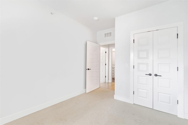 unfurnished bedroom with baseboards, visible vents, light carpet, and a closet