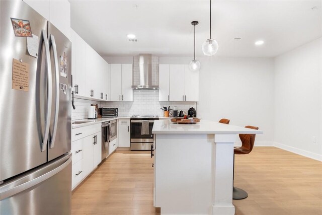 kitchen featuring light wood finished floors, a breakfast bar, stainless steel appliances, wall chimney range hood, and tasteful backsplash