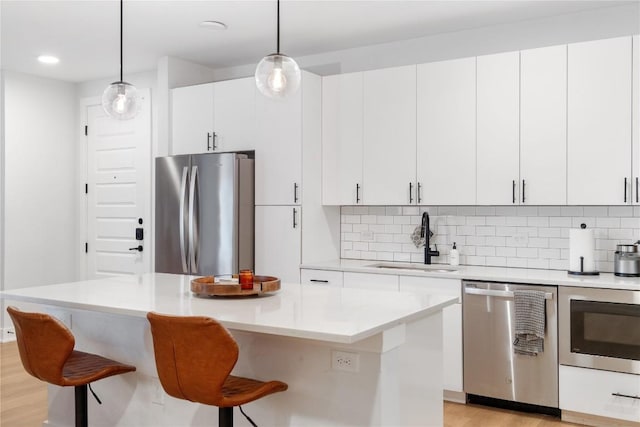 kitchen with a breakfast bar area, a sink, stainless steel appliances, light countertops, and tasteful backsplash