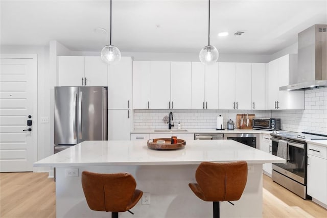 kitchen with wall chimney range hood, a breakfast bar area, light countertops, appliances with stainless steel finishes, and a sink