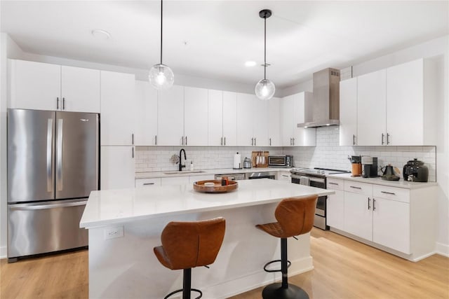 kitchen with light wood-type flooring, stainless steel appliances, wall chimney exhaust hood, and a sink