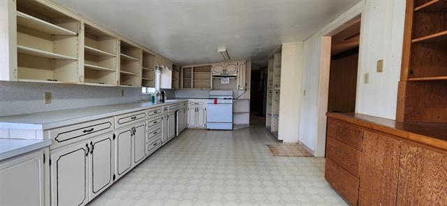 kitchen with open shelves, light floors, white cabinetry, light countertops, and stove