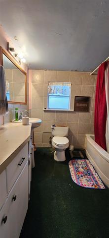 full bath with shower / bath combo with shower curtain, toilet, tile walls, and vanity