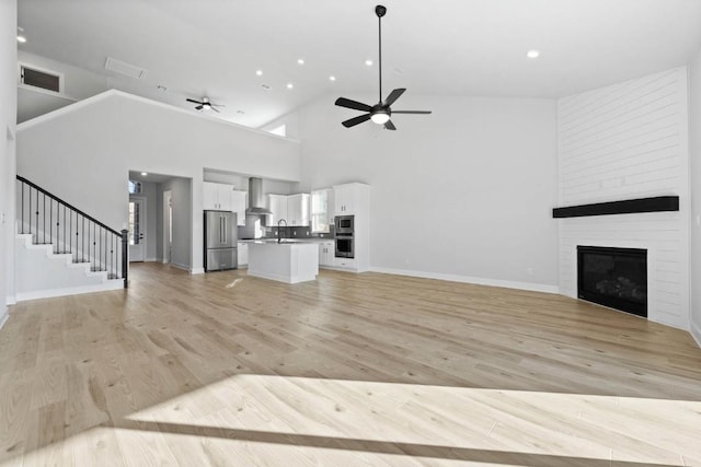 unfurnished living room with visible vents, stairway, light wood-type flooring, a ceiling fan, and a sink