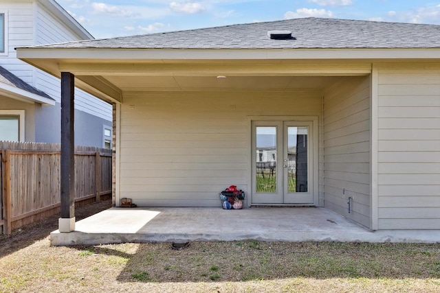view of exterior entry with a patio, french doors, roof with shingles, and fence