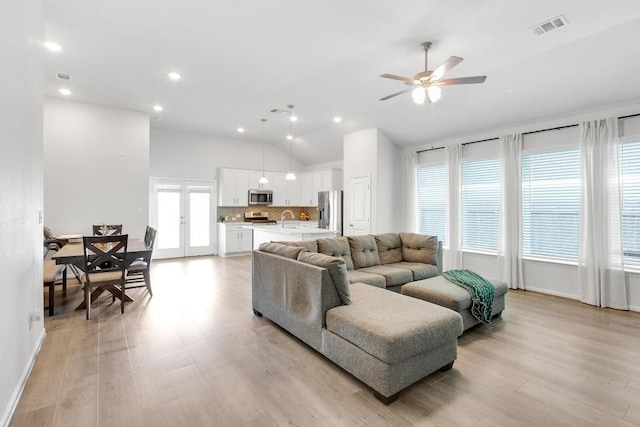 living room featuring light wood finished floors, visible vents, ceiling fan, and lofted ceiling