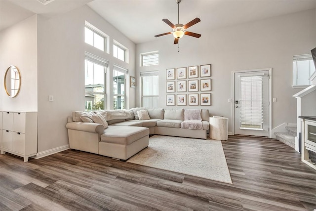 living room featuring ceiling fan, baseboards, a high ceiling, and dark wood-style floors