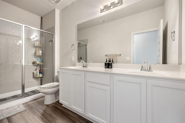 bathroom featuring toilet, a sink, wood finished floors, a shower stall, and double vanity