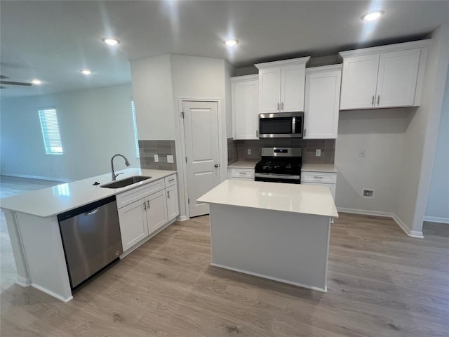 kitchen with light countertops, appliances with stainless steel finishes, a peninsula, light wood-style floors, and a sink