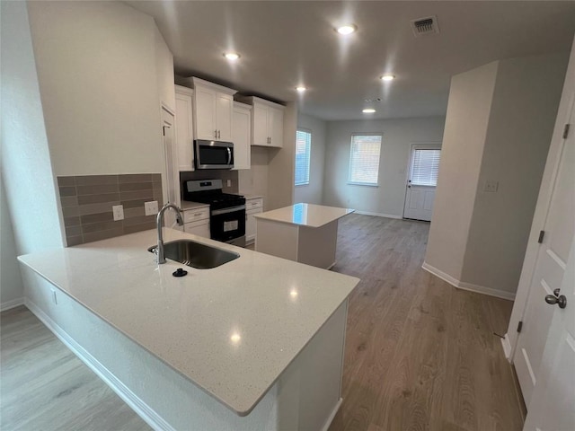 kitchen featuring visible vents, a kitchen island, a sink, stainless steel appliances, and light wood-type flooring