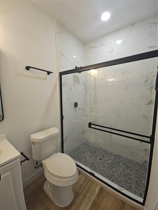 full bath featuring vanity, wood finished floors, baseboards, a marble finish shower, and toilet