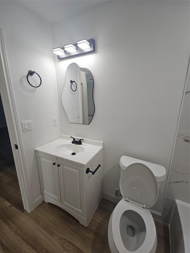 bathroom featuring baseboards, toilet, wood finished floors, and vanity